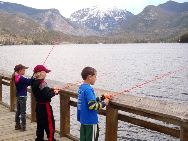 Children fishing from a deck with mountain view across the lake.
